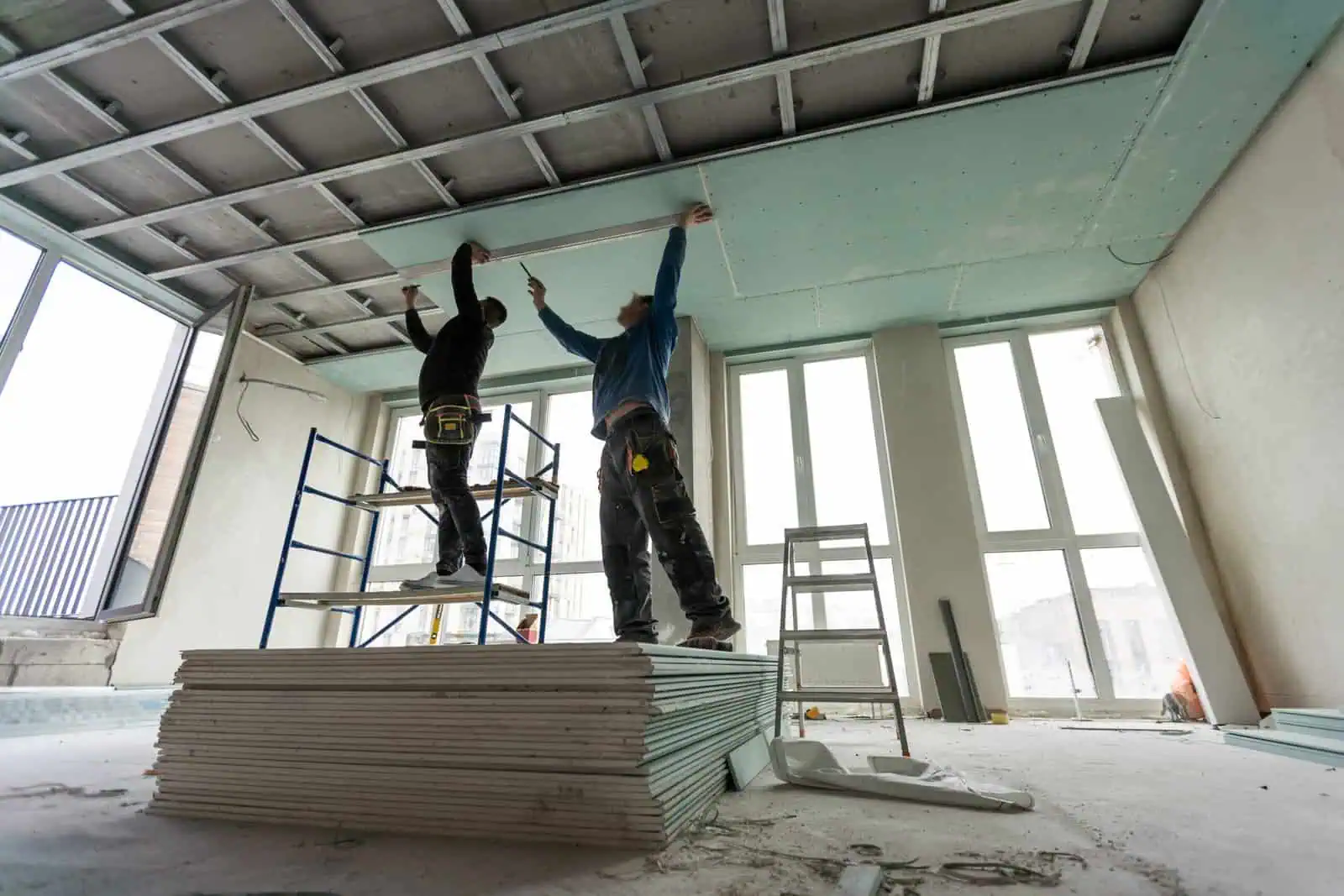 Two workers installing drywall on ceiling in a new construction site.