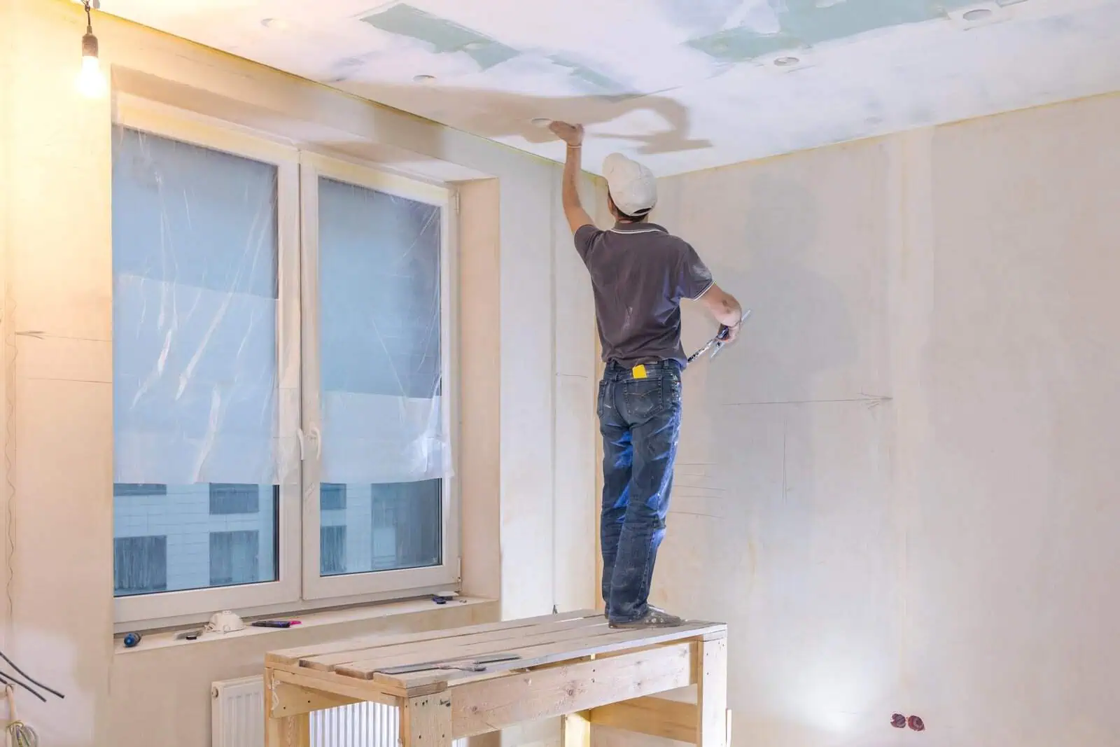 Drywall installer applying joint compound to ceiling in a residential room.